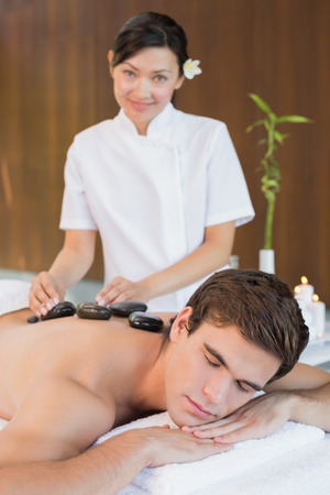 Close up of a handsome young man receiving stone massage at spa centerの写真素材