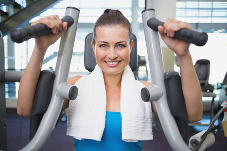 Fit brunette using weights machine for arms at the gym