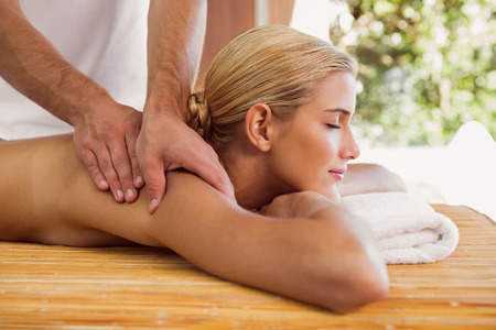Side view of an attractive young woman receiving shoulder massage at spa centerの写真素材