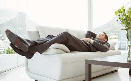 Full length of a young businessman lying on couch in living roomの写真素材
