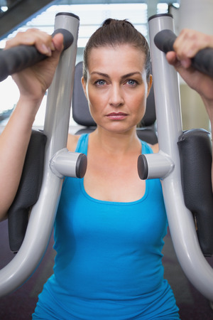 Fit brunette using weights machine for arms at the gym