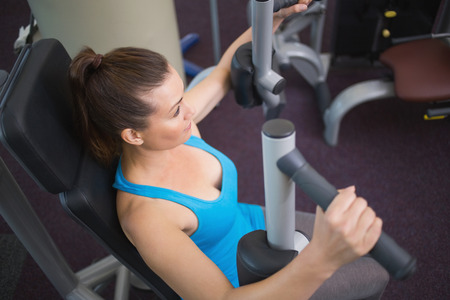 Fit brunette using weights machine for arms at the gym