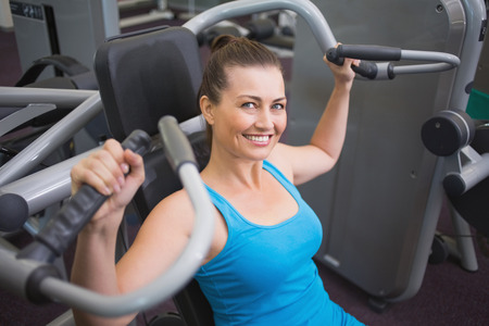 Fit brunette using weights machine for arms at the gym