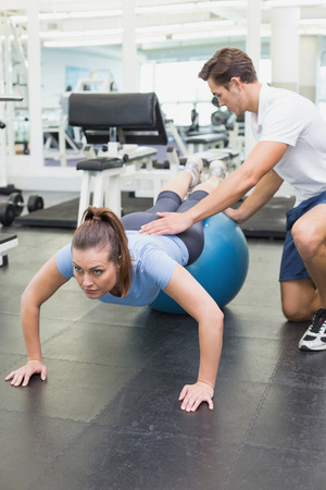 Personal trainer working with client on exercise ball at the gymの写真素材