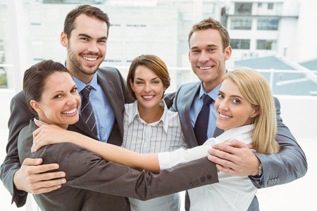 Portrait of happy young business people with arms around in office