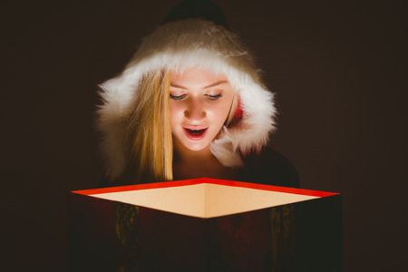 Festive blonde looking into glowing gift on black background