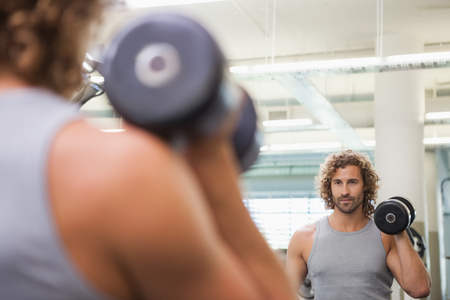 Reflection of a young muscular man exercising with dumbbell in the gymの写真素材
