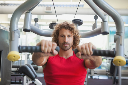 Portrait of a handsome young man working on fitness machine at the gym