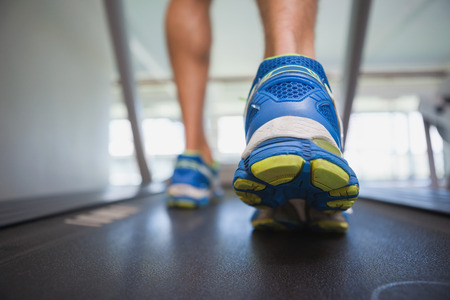 Rear view low section of a man running on treadmill in the gym