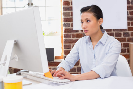 Concentrated young woman using computer at office deskの写真素材