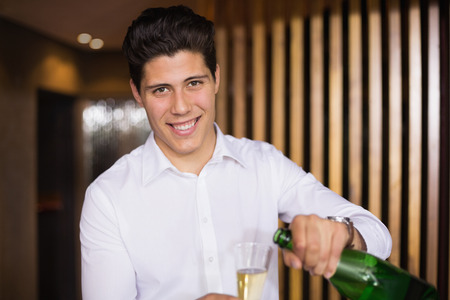 Handsome man smiling at camera pouring champagne at the barの写真素材