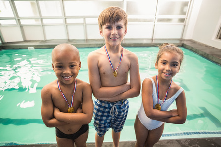 Cute swimming class smiling with medals at the leisure centerの写真素材