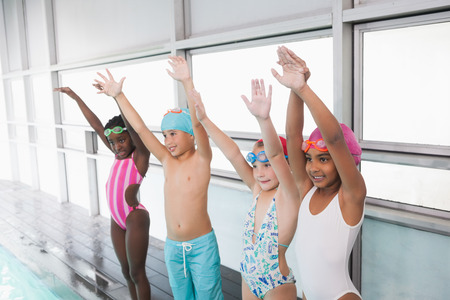 Cute little kids standing poolside with arms up at the leisure centerの写真素材