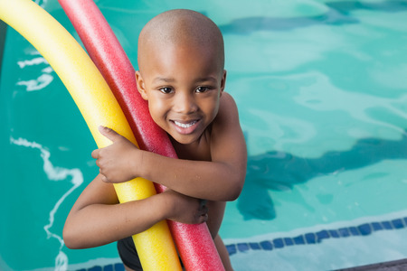 Cute little boy holding foam rollers by the pool at the leisure centerの写真素材