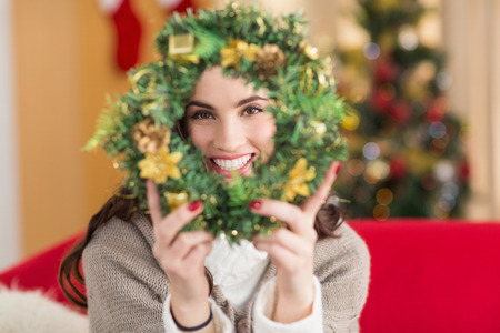 Brunette on the couch showing wreath at christmas at home in the living roomの写真素材