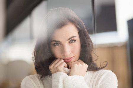 Brunette in white wool jumper smiling at camera at home in the living roomの写真素材