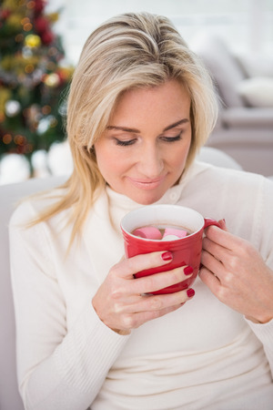 Blonde having hot chocolate on the couch at christmas at home in the living roomの写真素材
