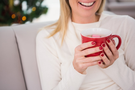 Blonde having hot chocolate on the couch at christmas at home in the living roomの写真素材