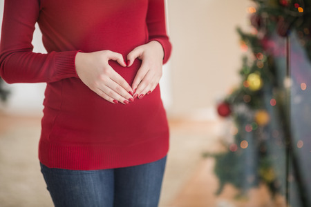 Close up of a pregnant woman making a heart on her belly at home in the living roomの写真素材