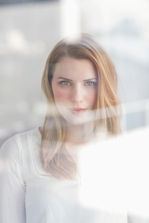 Thoughtful blonde woman looking at camera at home in the living roomの写真素材