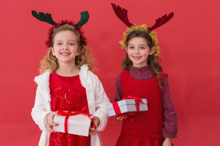 Festive little girls holding gifts on red backgroundの写真素材