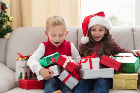 Festive siblings surrounded by gifts at home in the living roomの写真素材