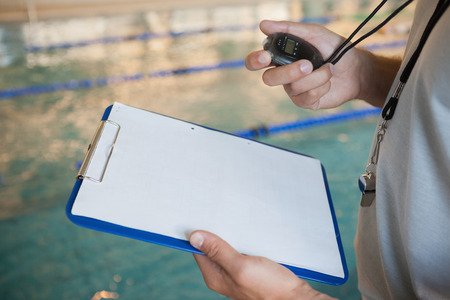 Swimming coach looking at his stopwatch by the pool at the leisure centerの写真素材