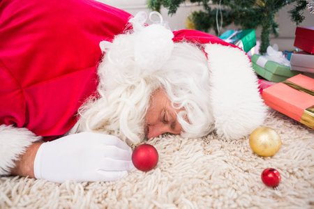 Exhausted santa resting on the rug near gifts and christmas treeの写真素材