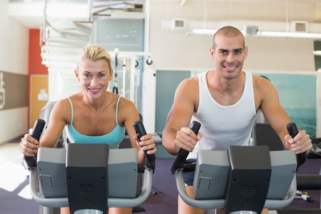 Portrait of a fit young couple working on exercise bikes at the gym