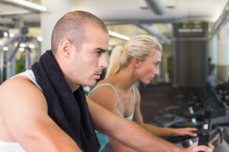 Side view of determined fit young couple working on exercise bikes at the gym