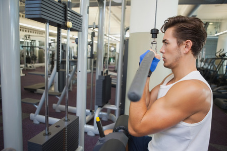 Fit man using weights machine for arms at the gym