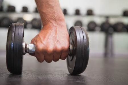 Fit man lifting heavy black dumbbell at the gymの写真素材