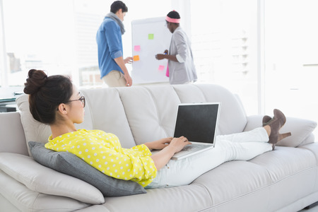 Young creative woman using laptop on couch in creative officeの写真素材