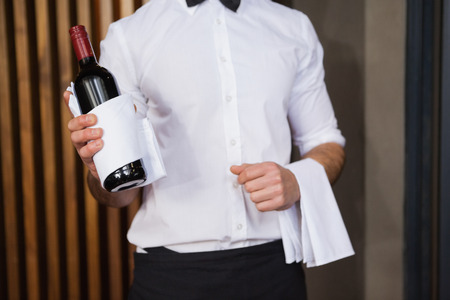 Handsome waiter holding a bottle of red wine and a towel in a barの写真素材