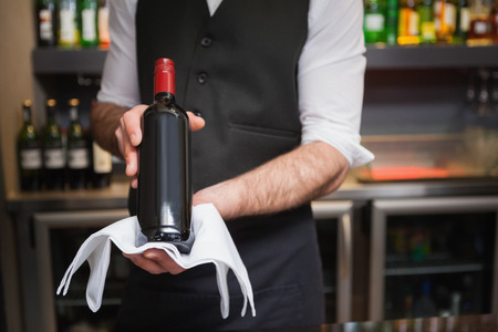 Handsome waiter holding a bottle of red wine in a barの写真素材