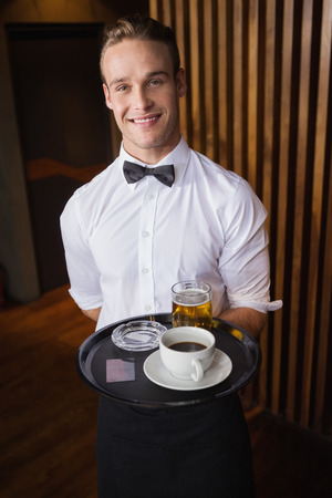 Smiling waiter holding tray with coffee cup and pint of beer in a barの写真素材