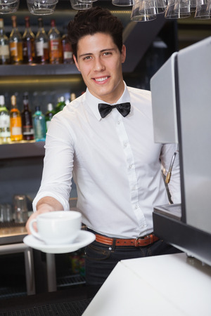 Young barista offering cup of coffee smiling at camera in a cafeの写真素材