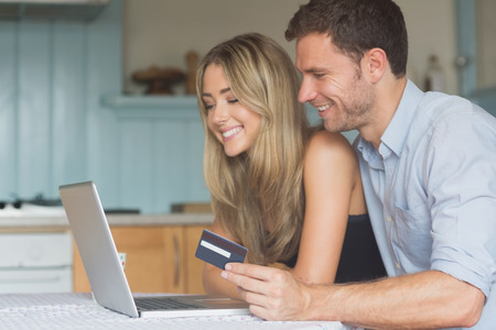 Cute couple using laptop together to shop online at home in the kitchenの写真素材