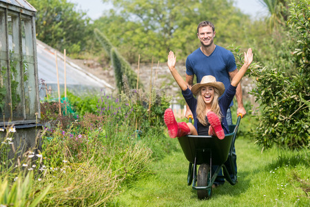 Man pushing his girlfriend in a wheelbarrow at home in the gardenの写真素材