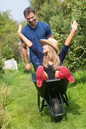 Man pushing his girlfriend in a wheelbarrow at home in the gardenの写真素材
