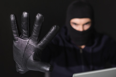 Hacker in balaclava with fingers spread out on black backgroundの写真素材