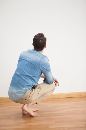 Casual man crouching on floor looking at wall at home in the living roomの写真素材