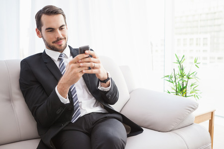 Businessman sending a text on the couch at home in the living roomの写真素材