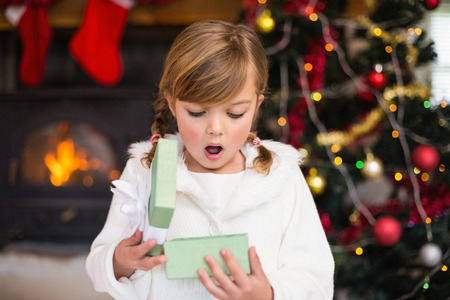 Shocked little girl opening a gift at home in the living roomの写真素材