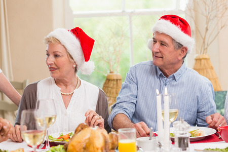 Cute mature couple in santa hat at christmas dinner at home in the living roomの写真素材