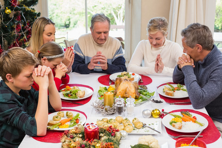 Extended family saying grace before christmas dinner at home in the dining roomの写真素材