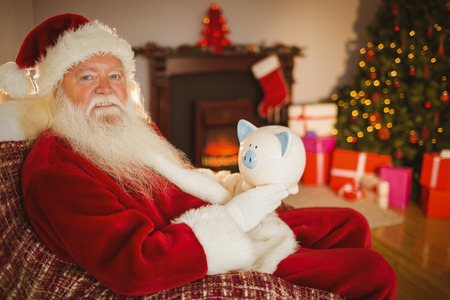 Santa claus holding piggy bank at home in the living roomの写真素材