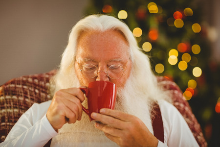 Father christmas drinking hot beverage at home in the living roomの写真素材