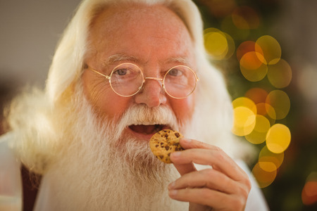 Happy santa claus eating a cookie at home in the living roomの写真素材