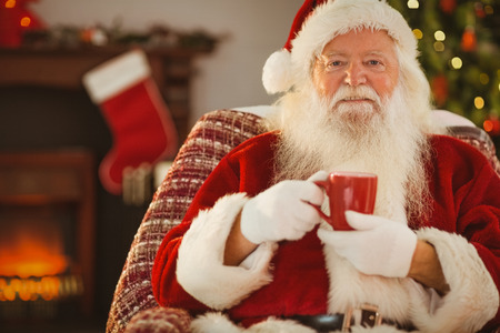 Smiling santa claus holding a mug at home in the living roomの写真素材